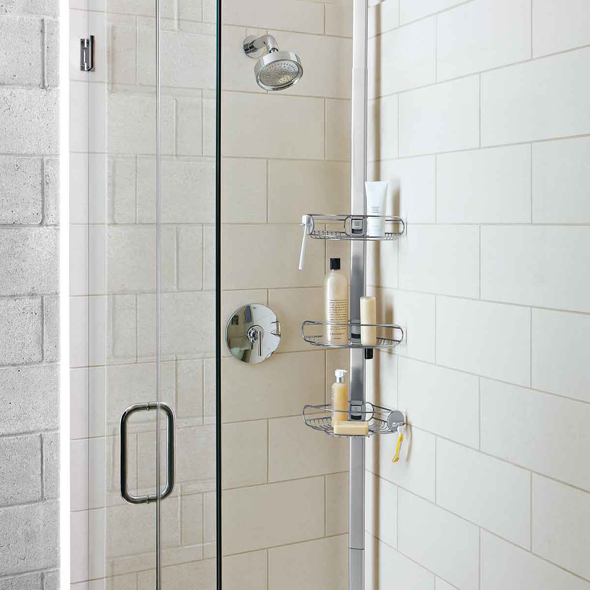 Angled view of Simplehuman Polished Stainless Steel Tension Shower Caddy, 3 adjustable shelves for shower organization.
