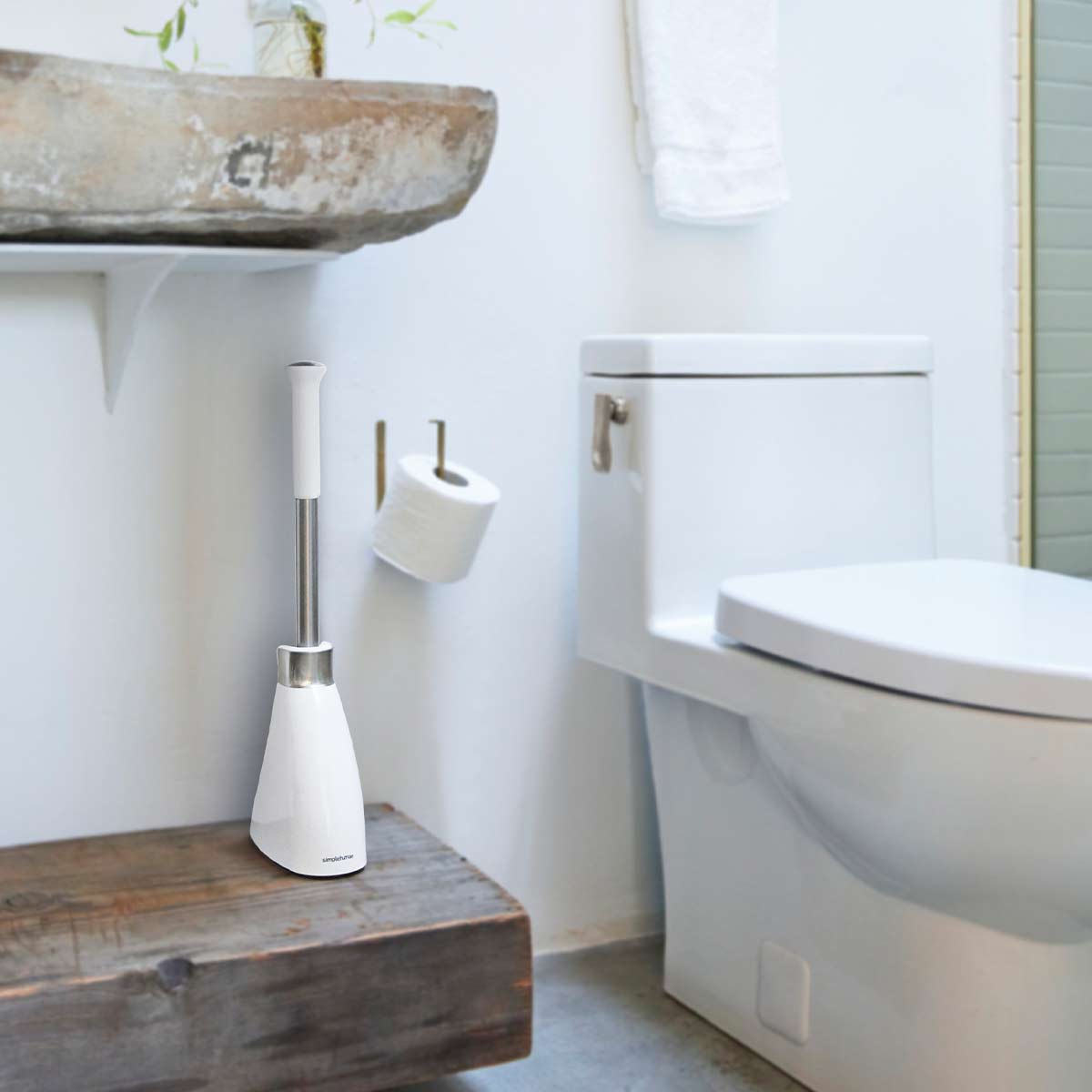 Simplehuman Toilet Brush in White/Stainless Steel on wooden stand in bathroom, featuring a raised easy-grip handle.