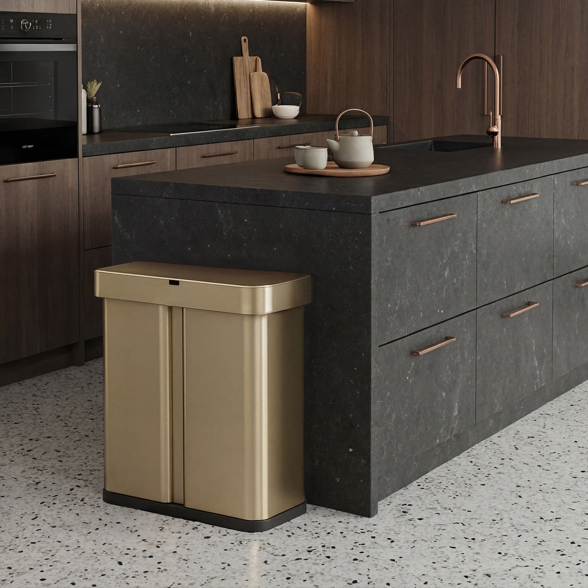 Simplehuman's Matte Gold Sensor Recycler along a black marble counter top with rose gold appliances and a few kitchen accessories.